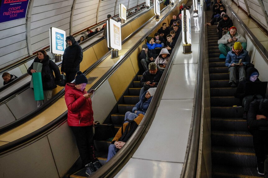 Ukraińcy siedzą na schodach ruchomych na stacji metra 