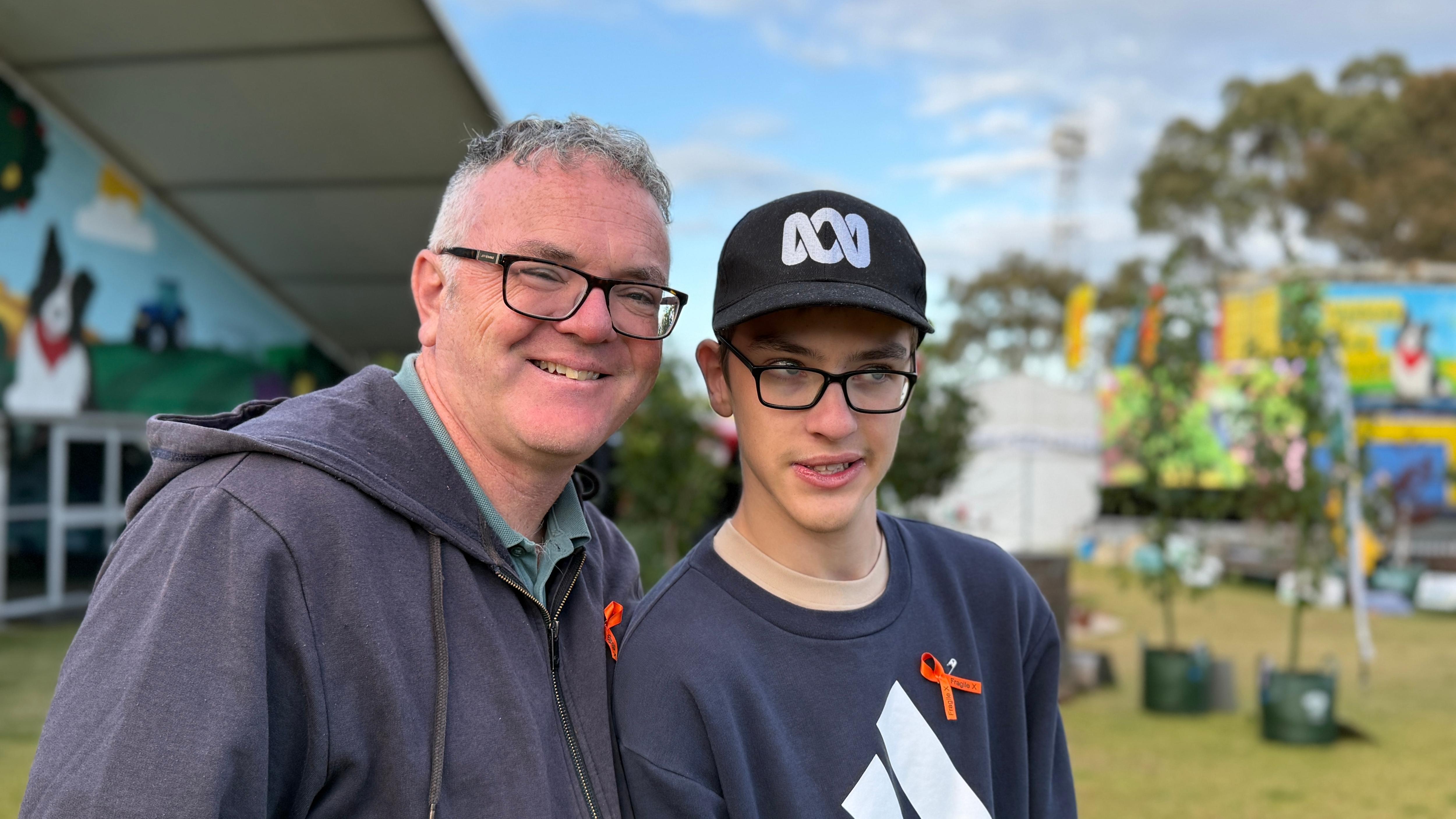 A man and his teenage son, wearing an ABC hat, smile together.