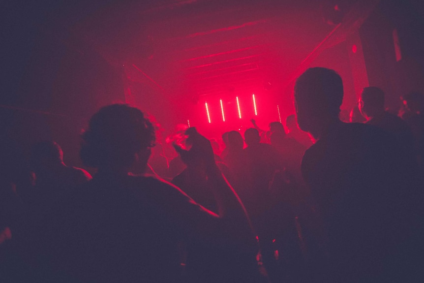 Silhouettes of people dancing in a nightclub bathed in red light.
