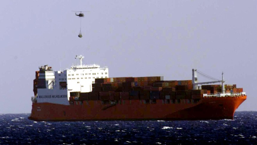 A large red shipping container from afar, sailing on the open ocean.