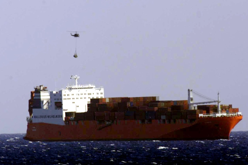A large red shipping container from afar, sailing on the open ocean.