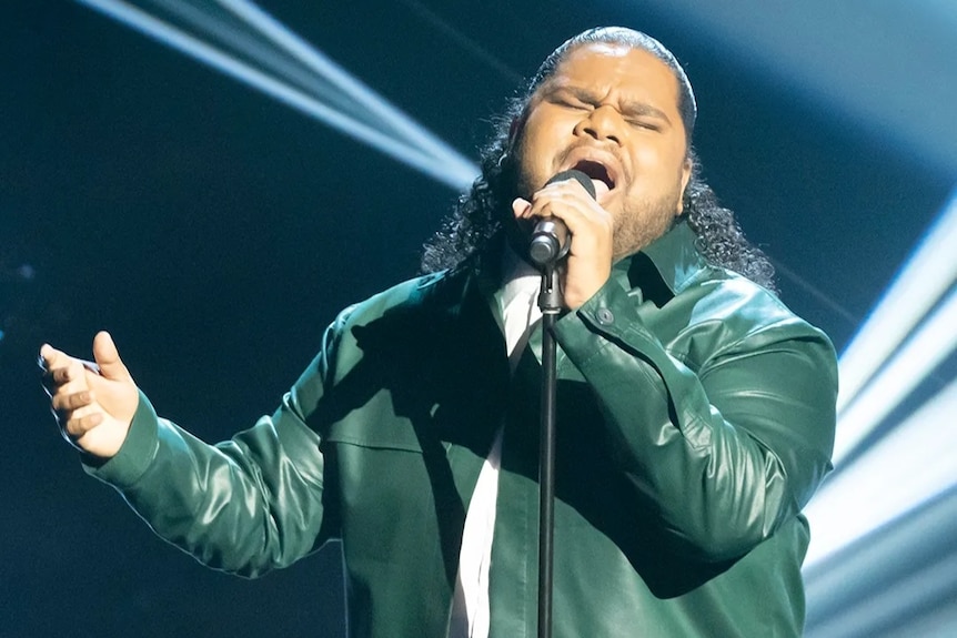 Man singing into microphone wearing green leather jacket