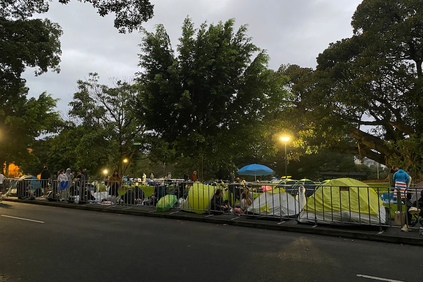 A line of tents and people behind a fence in the early morning