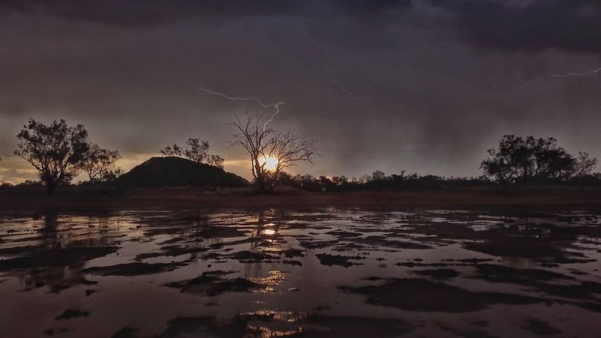 Lightning strike above a muddy claypan with water puddles.