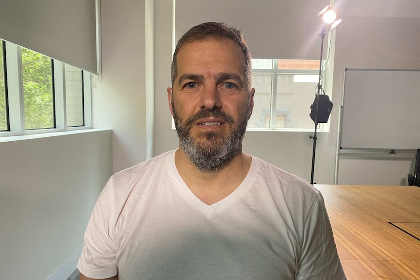 A headshot of a man in a white t-shirt