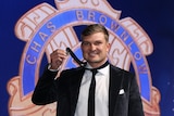 A Port Adelaide AFL player smiles at the camera and holds the Brownlow medal as it sits around his neck.