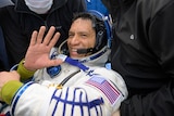 A man in a space suit waves.