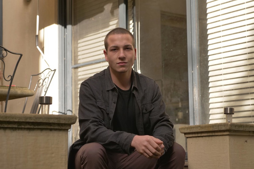 A young man with a shaved head looks serious.