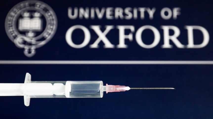 Medical syringe is seen with the University of Oxford logo displayed on a screen in the background