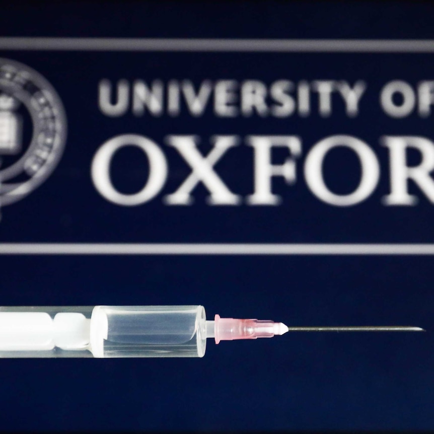 Medical syringe is seen with the University of Oxford logo displayed on a screen in the background