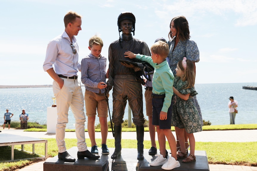 Man and son on left and woman on right with two boys and girl looking at bronze life size jockey statue in the middle