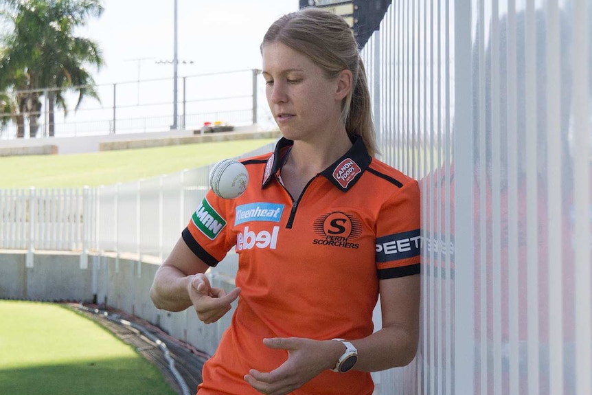 A wide shot of cricketer Jemma Barsby standing on the WACA Ground in a Perth Scorchers shirt tossing a cricket ball.