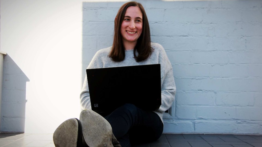 a woman sitting in the sun with a laptop smiling