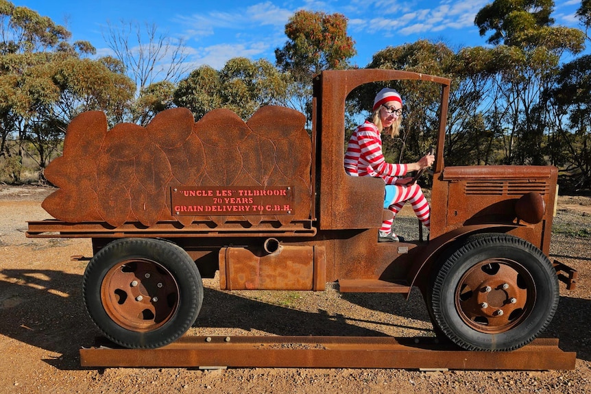 A woman in a white-and-red-striped shirt sitting in a sculpture of a truck.