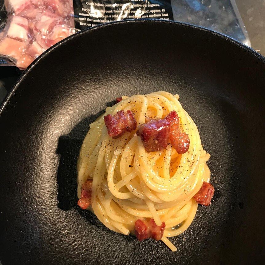 A pan with spaghetti and lamb bacon on top with pepper.