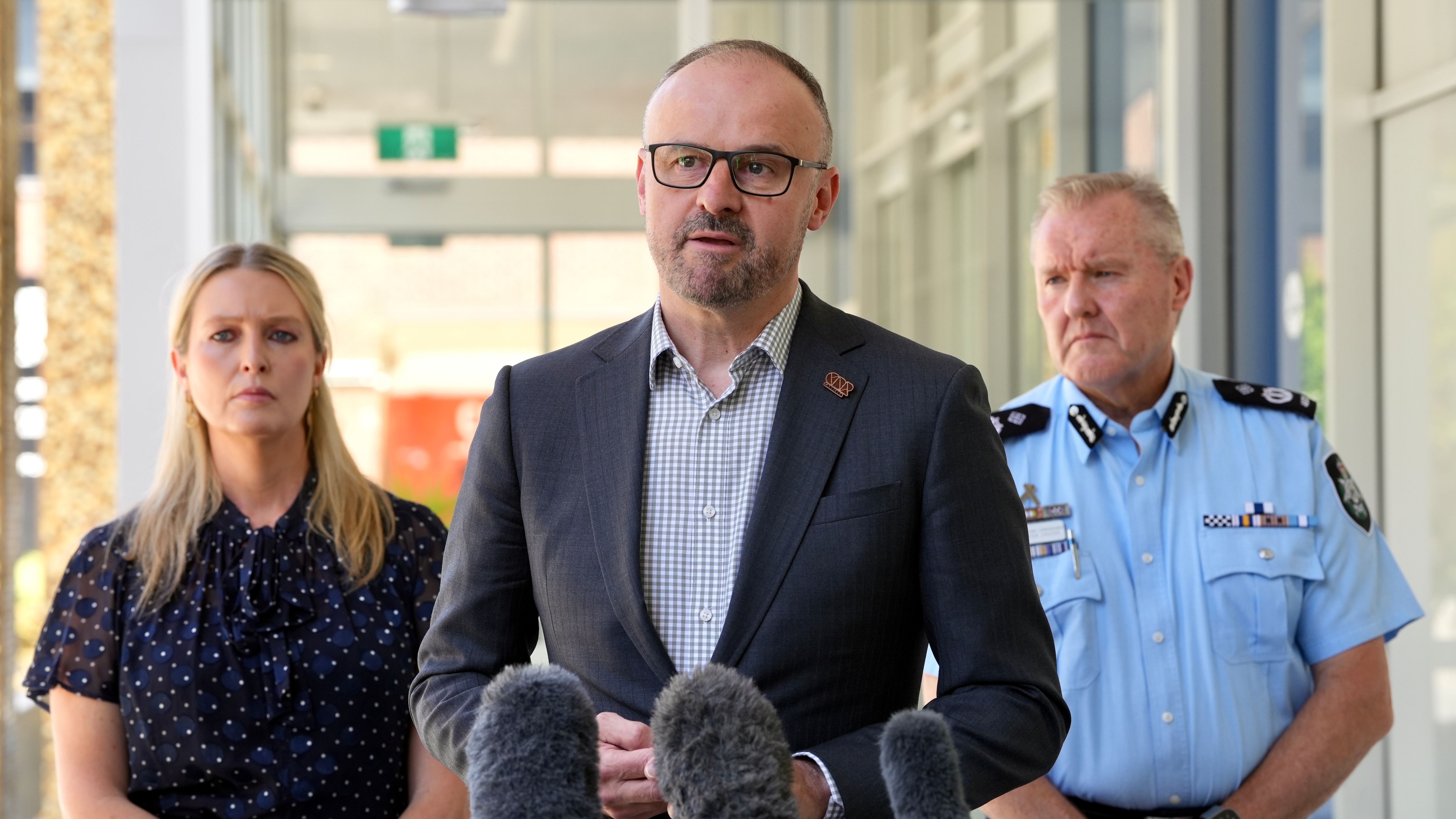 Barr parece serio, de pie frente a un micrófono en medio de su discurso, con dos personas detrás de él, incluido un oficial de policía.