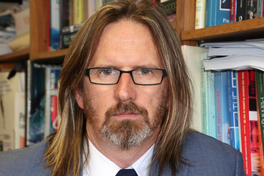 Paul Maginn, urban and regional planning expert from UWA, standing in front of a bookshelf.
