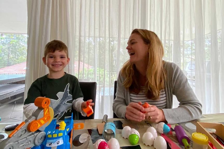 A mother laughs as she sits with her son in their home.