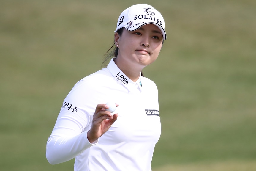 A South Korean female professional golfer holds up a ball after sinking a putt.