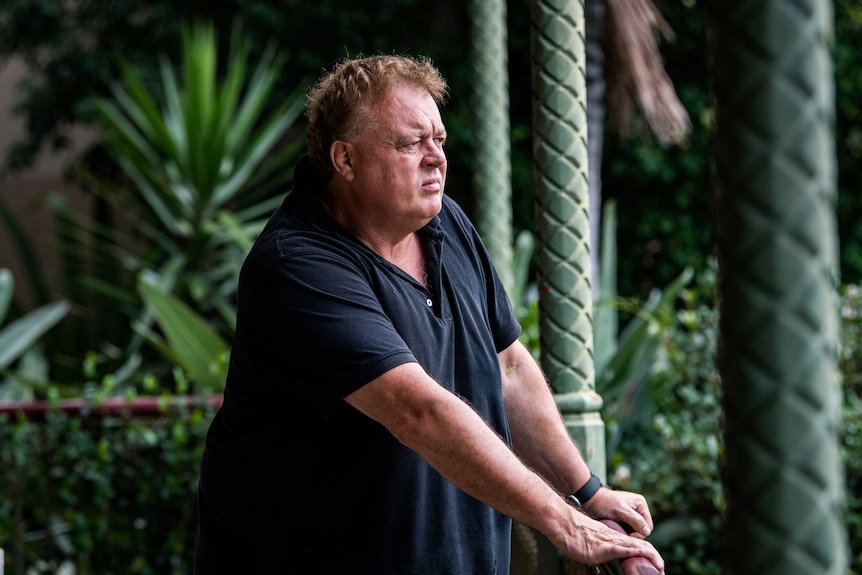 A man leans on a balcony and looks into the distance.