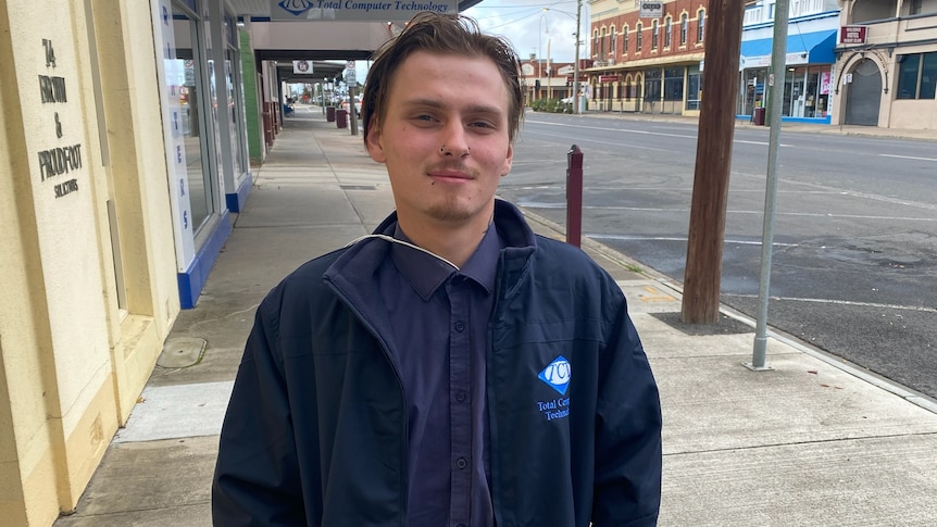 A young man standing on the footpath of a country town main street.