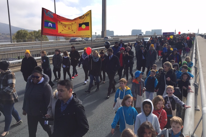People walking across a bridge with Aboriginal and Torres Strait Island banners