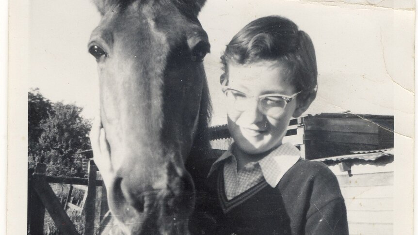 A black and white photo of an 11-year-old girl wearing glasses hand feeding a horse.