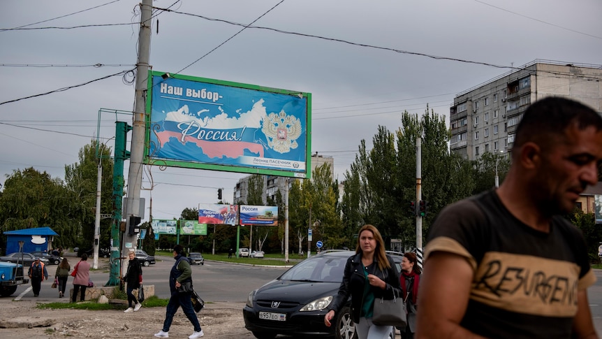 people walk by a large blue billboard in an urban street