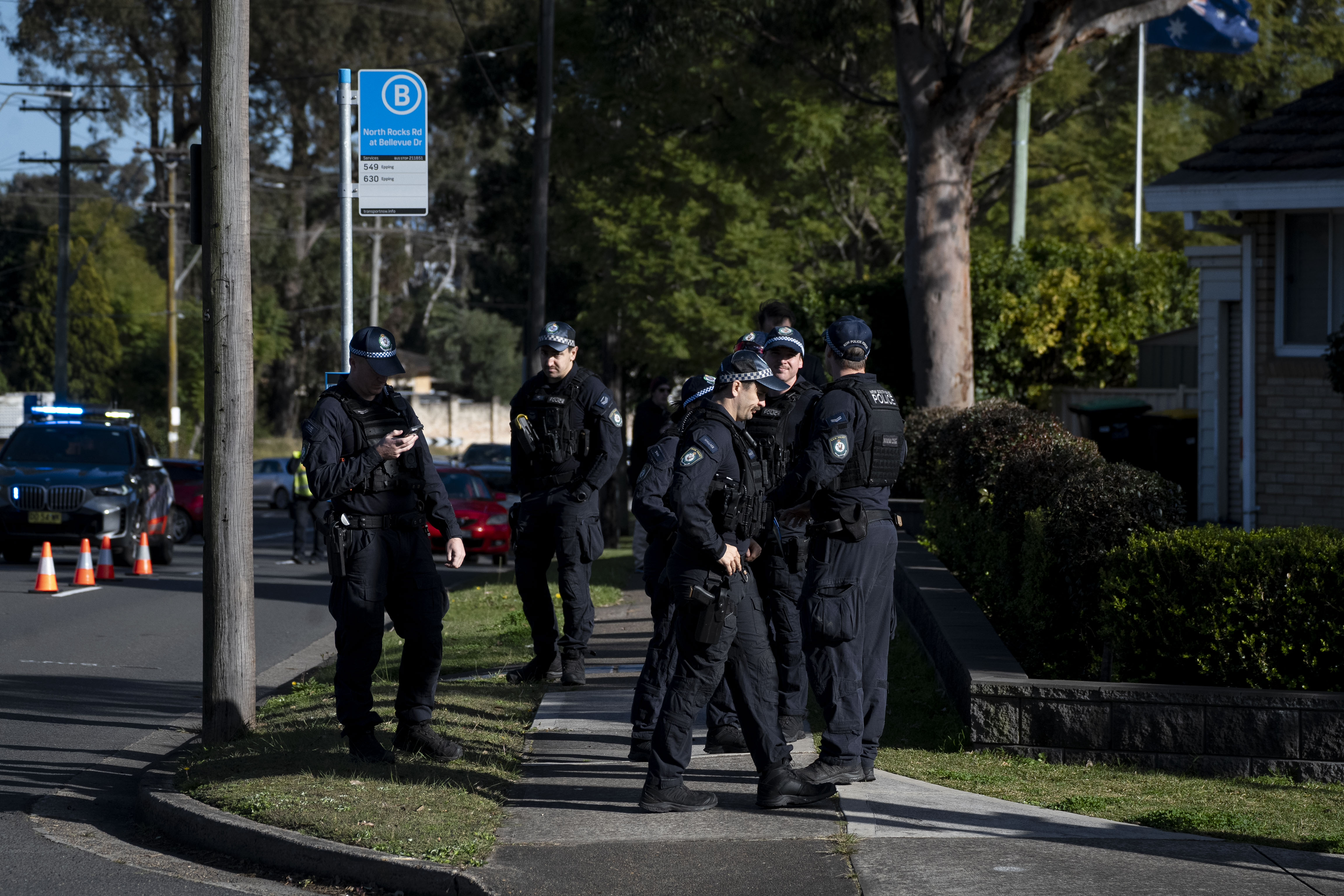 A group of police officers in dark uniforms stands near a bus stop on the street.