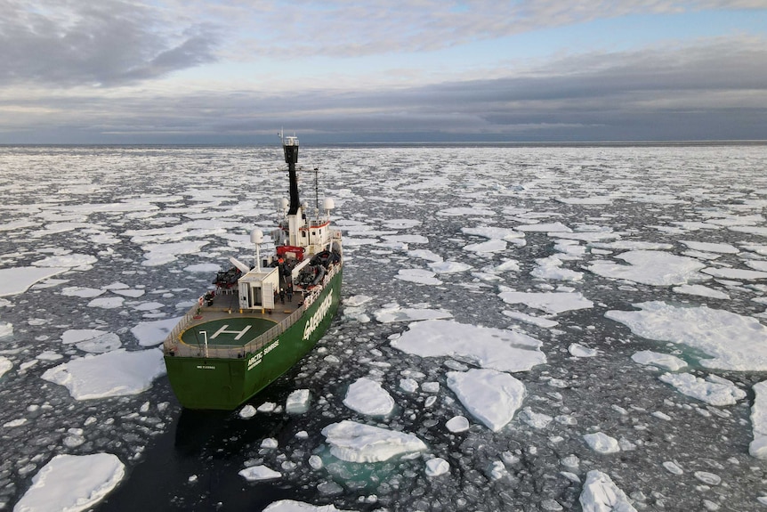 An aerial shot of a ship as it sails through broken up sea ice.