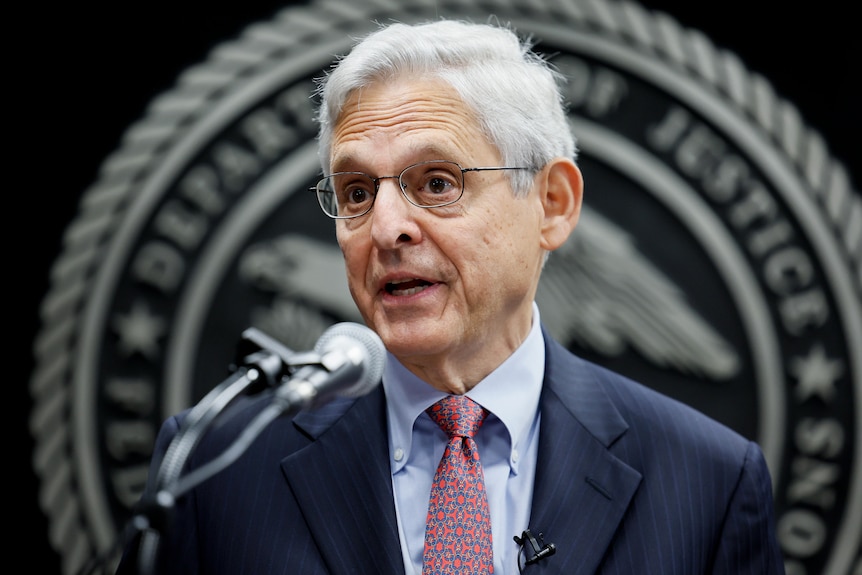 Attorney General Merrick Garland is speaking into a microphone with his eyebrows raised.