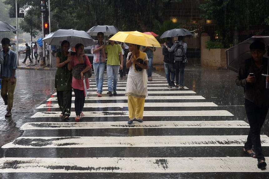 Indian pedestrians cross the road in a heavy downpour in Mumbai