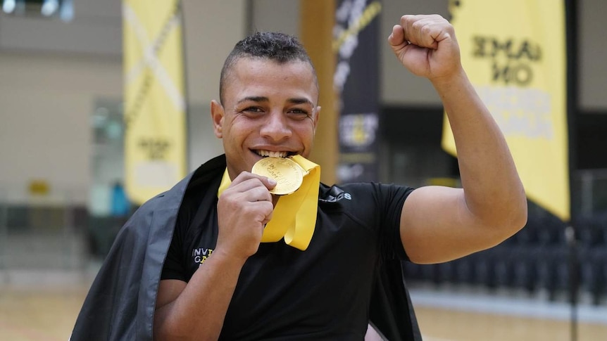 man smiling and holding a gold medal up to his mouth with his fist raised in triumph