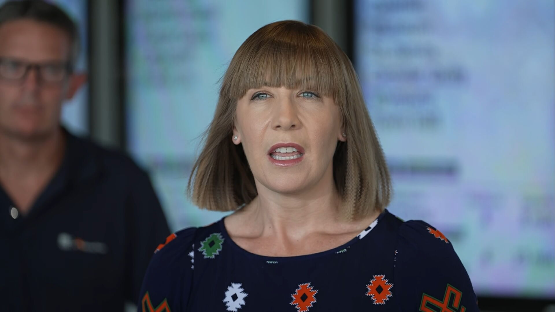 Una mujer con un corte bob y el pelo hasta los hombros parada frente a las líneas del tren.