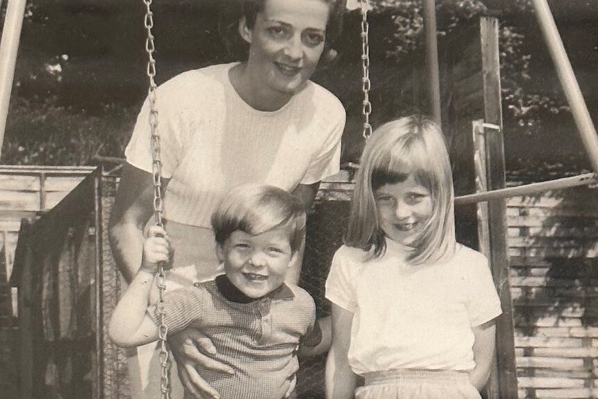 A black and white photo of a woman with a boy and girl on a swing 