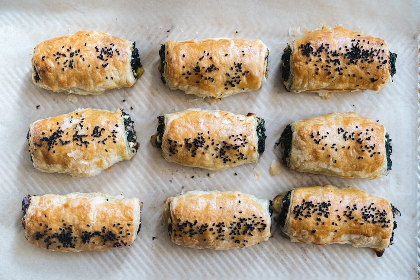 Bird's eye view of baked spinach-filled pastry rolls on a paper-lined baking tray.