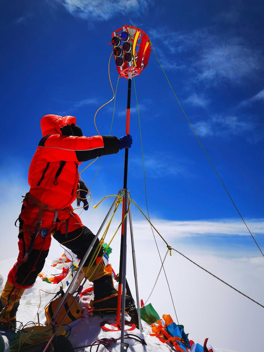 Person in red snow jacket holds equipment on snowy peak.