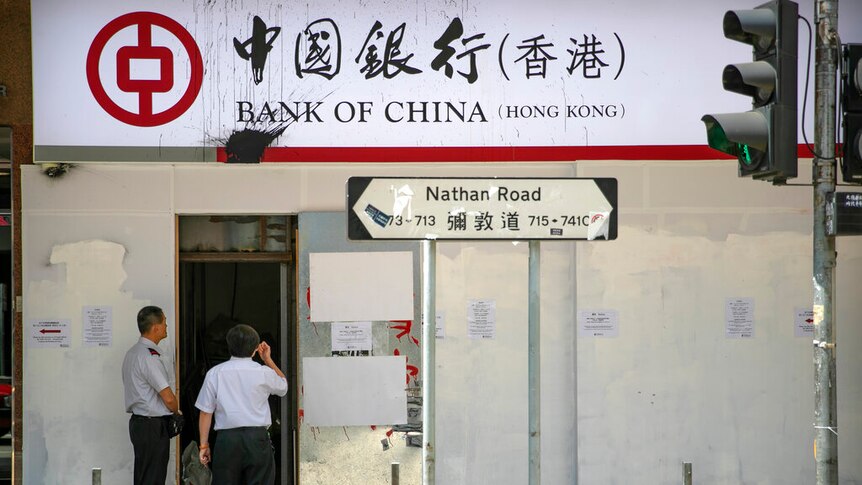 You view a Bank of China shopfront that is covered in metal barricades flanked by two security guards.