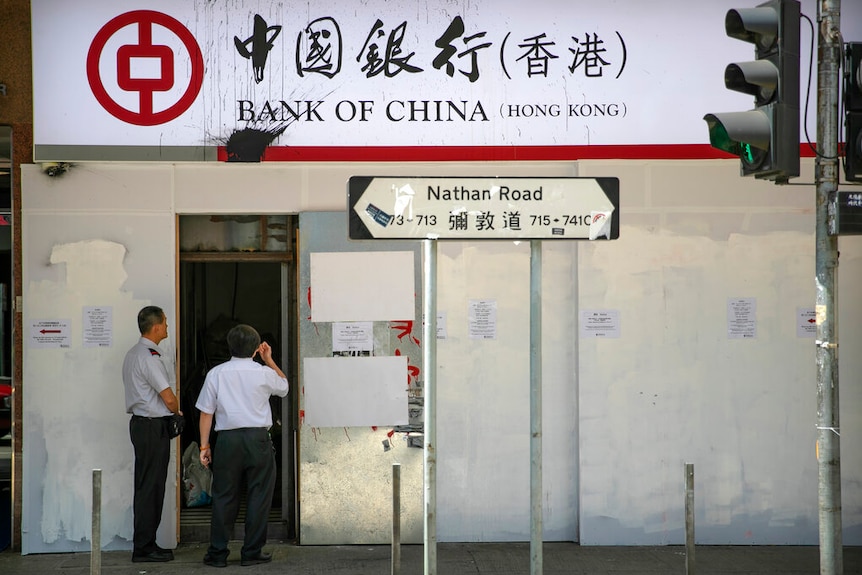 You view a Bank of China shopfront that is covered in metal barricades flanked by two security guards.