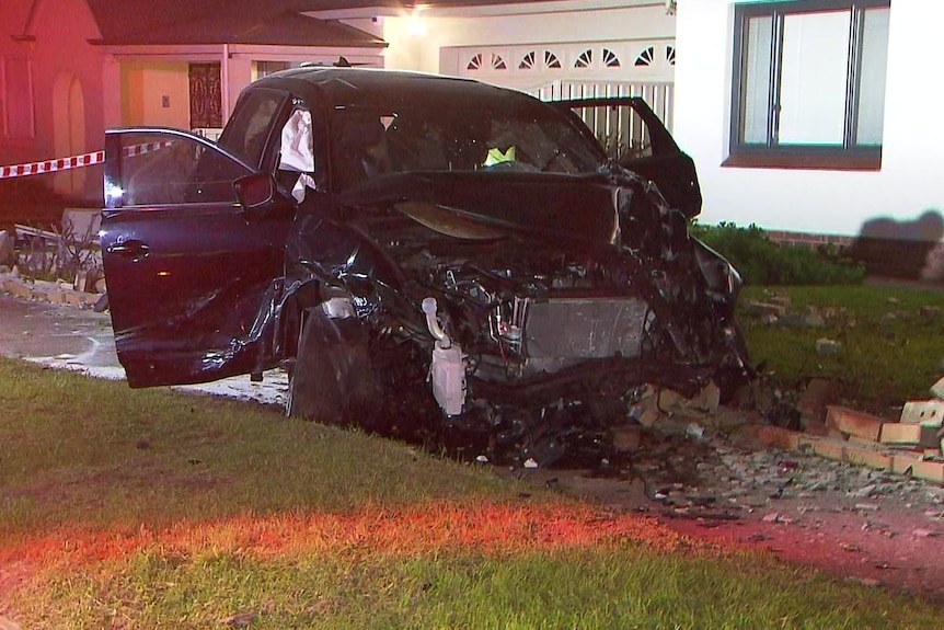 A damaged car sits in the front yard of a suburban house. 