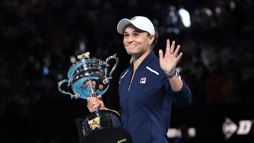 Woman in sportswear holds large silver trophy and smiles humbly toward crowd