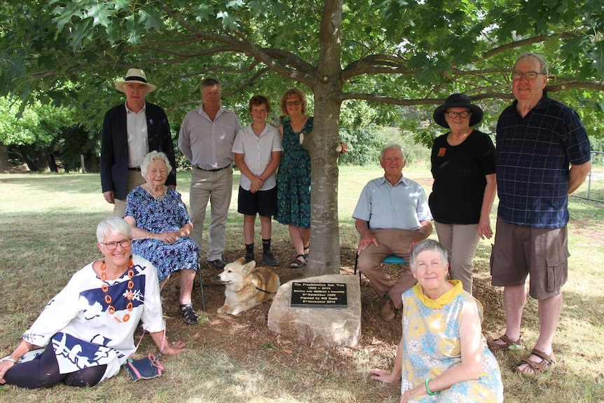 Ten locals gather around the proclamation plaque under an oak tree while looking at the camera.