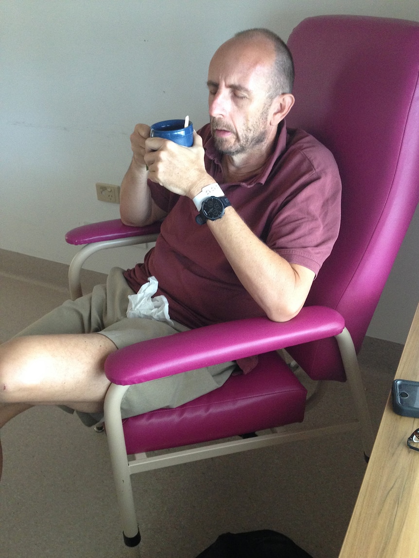 Darren Lydeamore sitting on a hospital chair drinking tea with eyes closed.