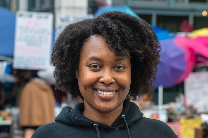 Woman with dark curly hair wearing black hoodie holding a coffee cup