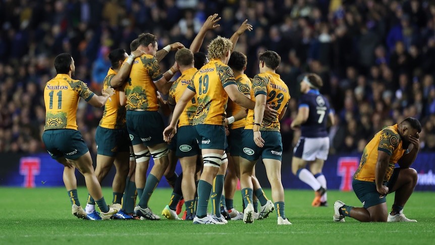 A group of tired but happy Australian rugby union players celebrate on the field after winning a Test match.