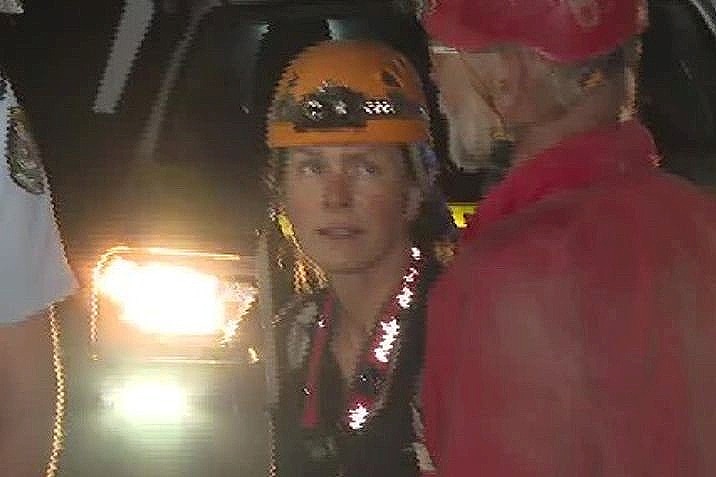 a woman wearing a hard hat stand outdoors at night after being rescued from a cave where she was trapped