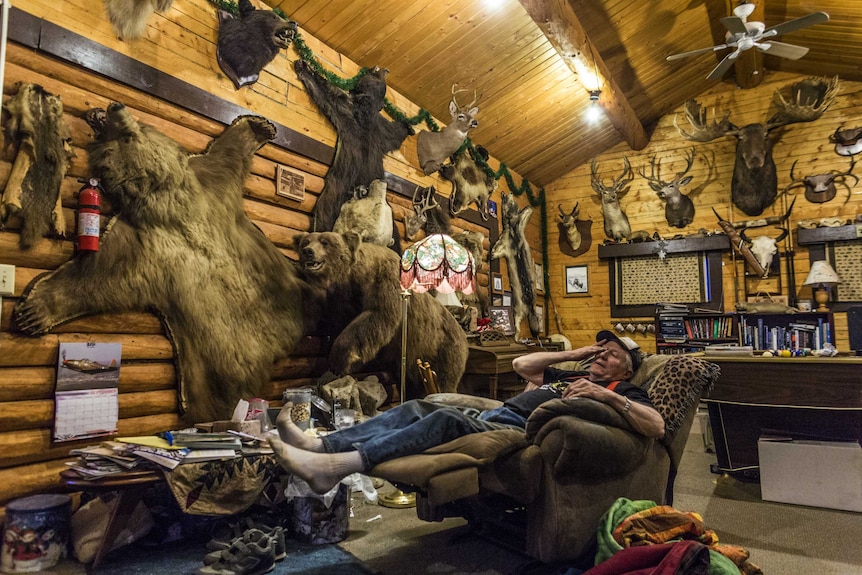 A hunter relaxing on a couch in a cabin with animal heads mounted on the walls.