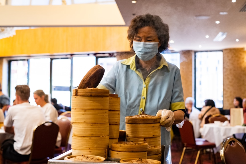 a woman lifts a lift of a round yum cha container that is on top of a trolley