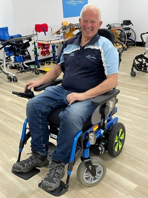 Cary Nathan sits in a wheelchair surrounded by mobility equipment