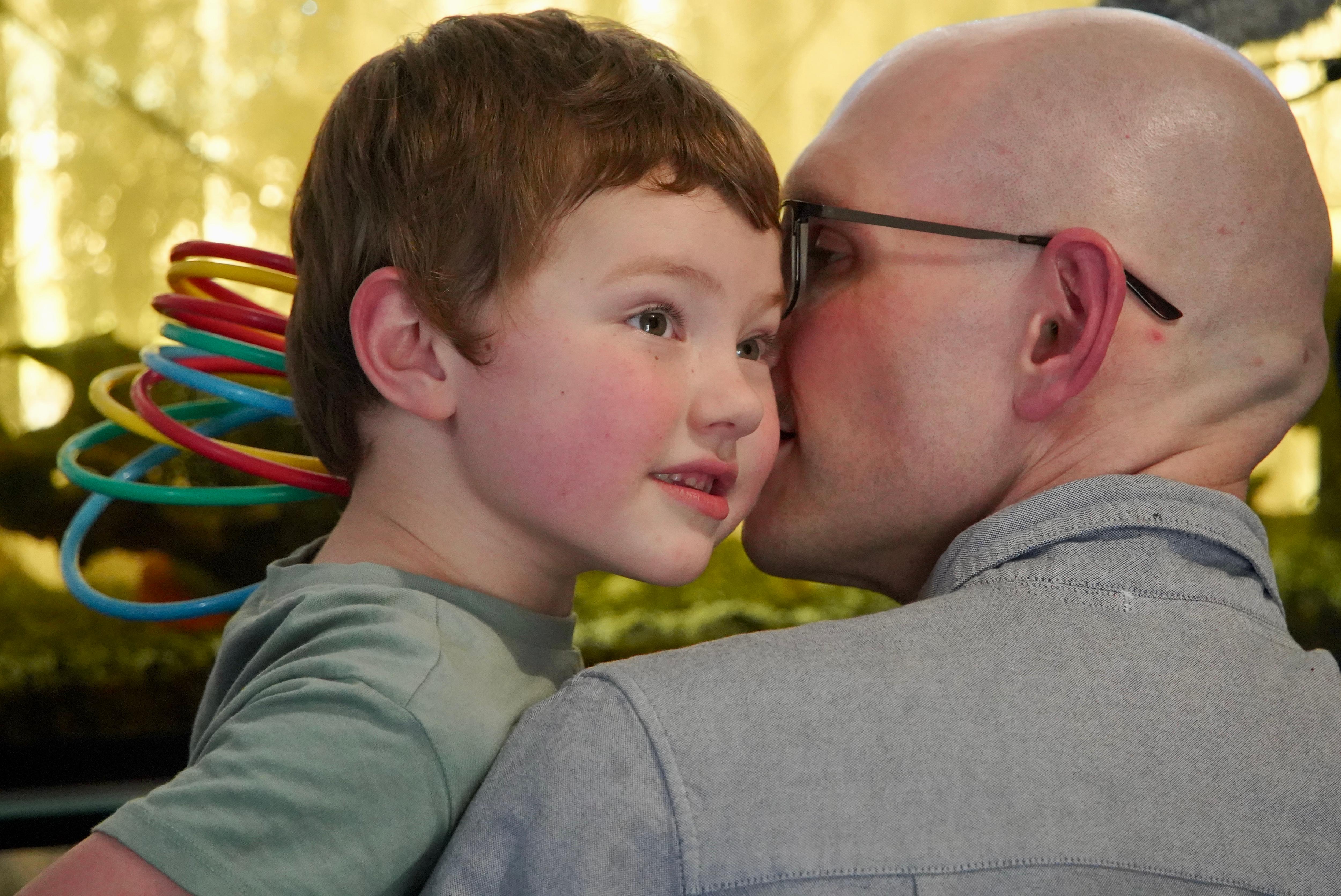 A young boy looks into the distance while held by his dad he looks towards him.